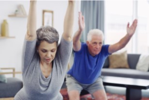 An aged man and a women excercising at home with their hands lifted